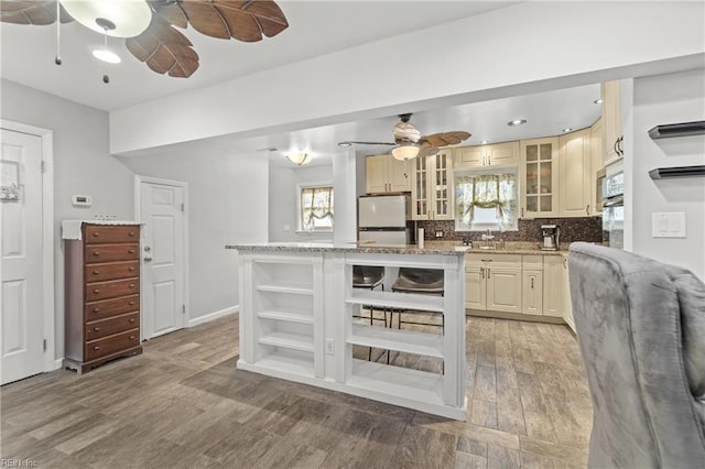 kitchen featuring ceiling fan, refrigerator, cream cabinets, light stone counters, and light hardwood / wood-style flooring