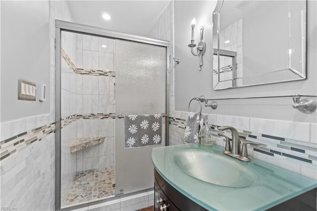 bathroom featuring walk in shower, vanity, and tile walls