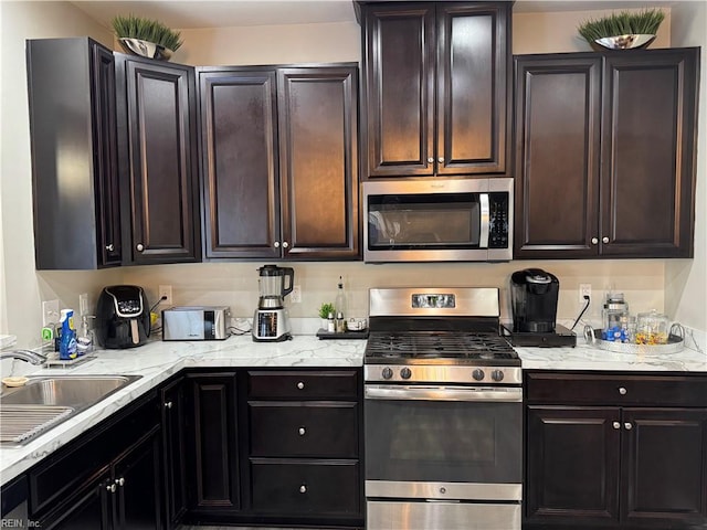 kitchen featuring sink, light stone counters, dark brown cabinetry, and appliances with stainless steel finishes