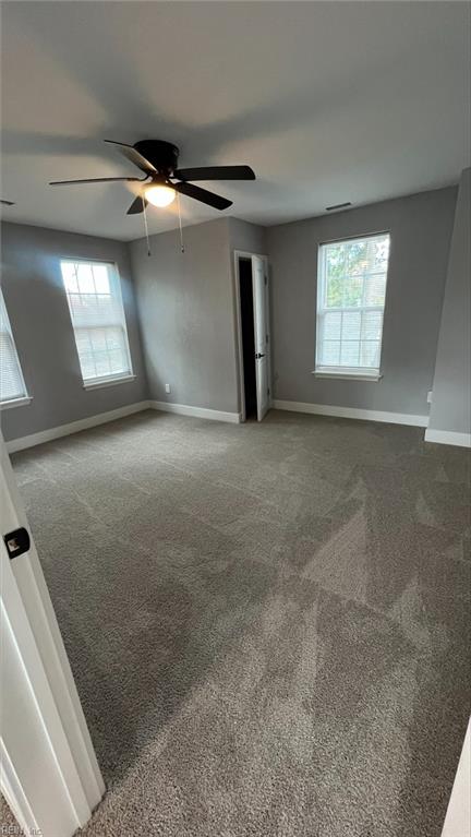 carpeted empty room with ceiling fan and plenty of natural light