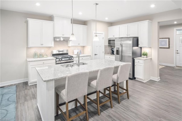 kitchen featuring decorative light fixtures, an island with sink, sink, white cabinets, and stainless steel appliances