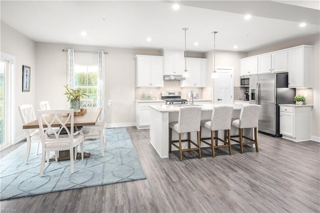 kitchen with tasteful backsplash, a center island with sink, pendant lighting, stainless steel appliances, and white cabinets