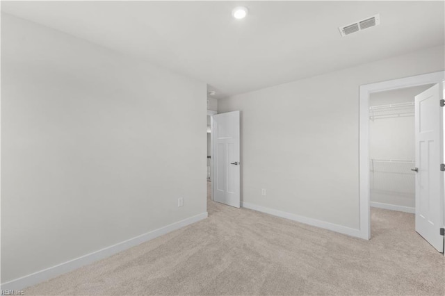 unfurnished bedroom featuring a walk in closet, a closet, and light carpet