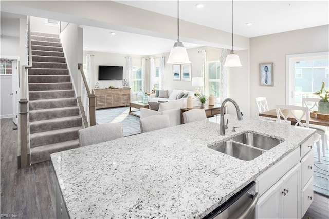 kitchen with pendant lighting, sink, white cabinets, light stone countertops, and a center island with sink