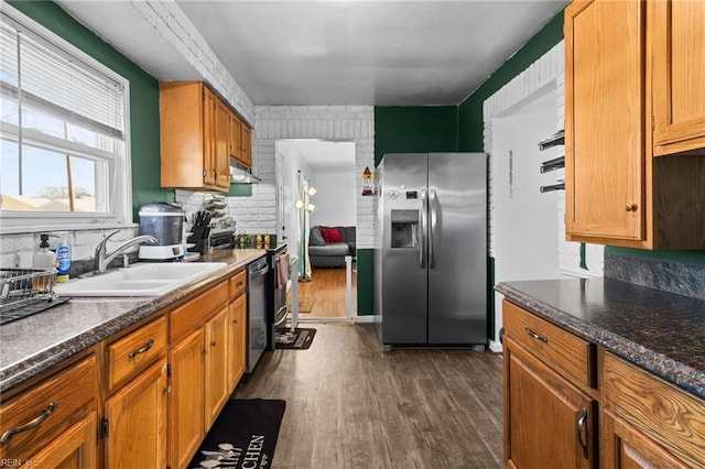 kitchen with appliances with stainless steel finishes, sink, backsplash, dark wood-type flooring, and dark stone countertops