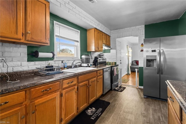 kitchen featuring exhaust hood, sink, dark stone countertops, stainless steel appliances, and dark hardwood / wood-style floors