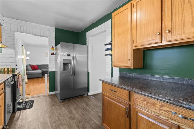 kitchen with stainless steel appliances, dark stone counters, and dark hardwood / wood-style flooring