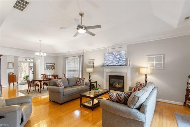 living room with ornamental molding, ceiling fan with notable chandelier, a wealth of natural light, and light wood-type flooring