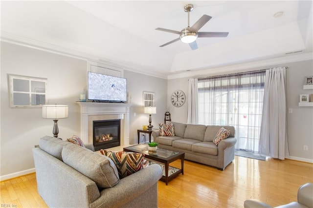 living room with light hardwood / wood-style floors, ornamental molding, and a raised ceiling