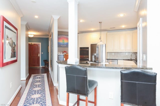 kitchen with kitchen peninsula, crown molding, ornate columns, dark stone countertops, and stainless steel appliances