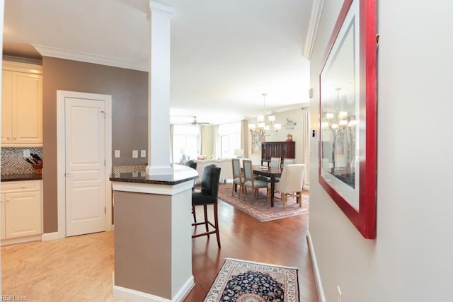 kitchen with crown molding, hanging light fixtures, ornate columns, backsplash, and a breakfast bar