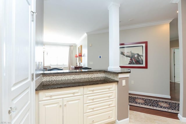 kitchen with cream cabinets, ornamental molding, ornate columns, and dark stone counters