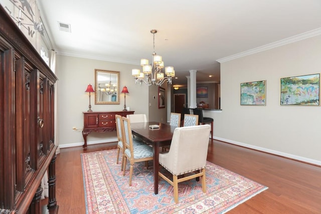 dining space featuring decorative columns, an inviting chandelier, crown molding, and dark hardwood / wood-style flooring