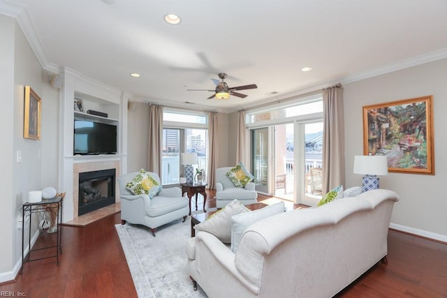 living room featuring dark wood-type flooring, a fireplace, built in features, ornamental molding, and ceiling fan