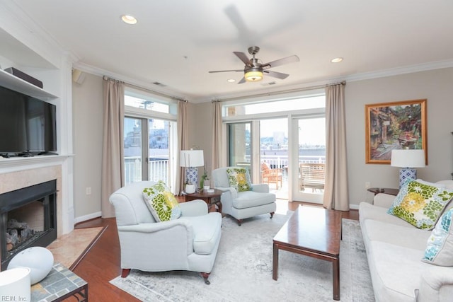 living room featuring hardwood / wood-style flooring, ceiling fan, crown molding, and a fireplace