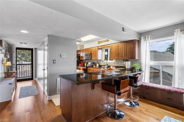 kitchen featuring light hardwood / wood-style floors, a textured ceiling, kitchen peninsula, a breakfast bar, and stainless steel appliances