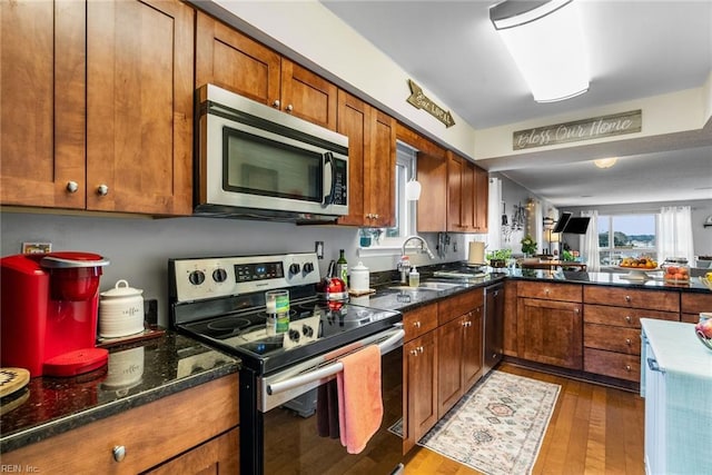 kitchen featuring sink, wood-type flooring, dark stone counters, and appliances with stainless steel finishes