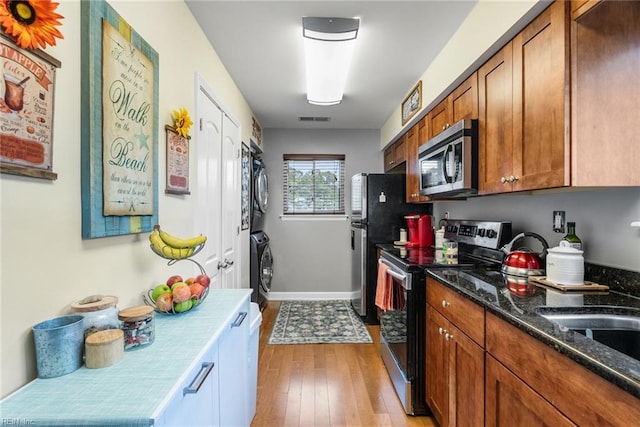 kitchen featuring dark stone countertops, appliances with stainless steel finishes, stacked washer and dryer, and light wood-type flooring