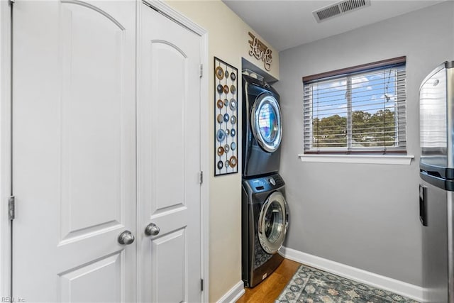 laundry area featuring wood-type flooring and stacked washer / dryer