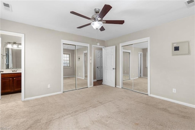 unfurnished bedroom with light carpet, ceiling fan, sink, two closets, and connected bathroom