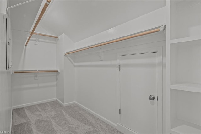 walk in closet with light colored carpet and vaulted ceiling