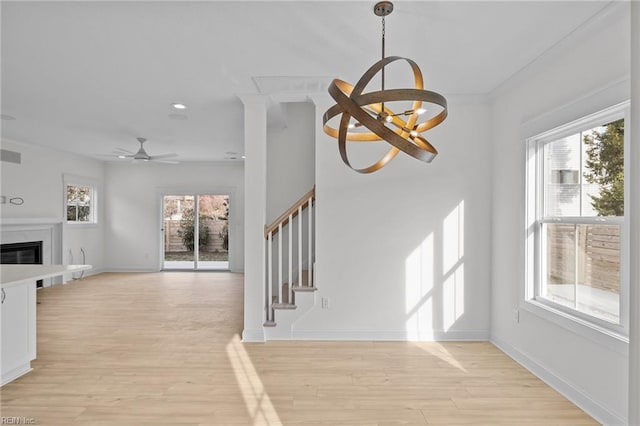 unfurnished living room with ceiling fan with notable chandelier, a high end fireplace, crown molding, and light hardwood / wood-style flooring