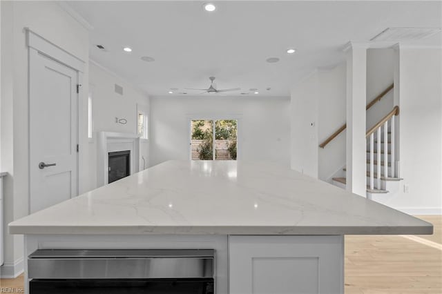 kitchen with a center island, white cabinetry, light stone countertops, light wood finished floors, and a glass covered fireplace