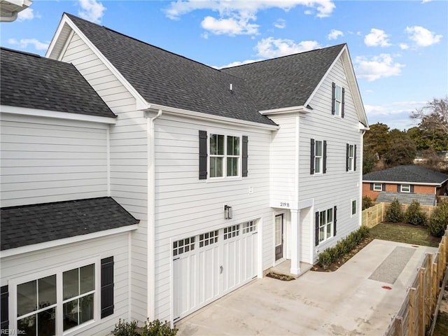 view of side of property with driveway, a shingled roof, and fence