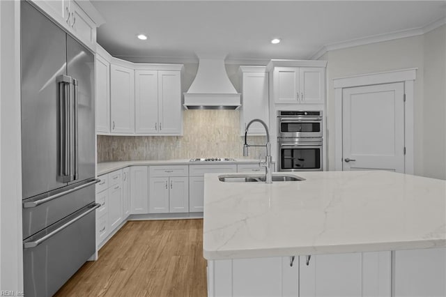 kitchen featuring premium range hood, light stone counters, white cabinets, and appliances with stainless steel finishes