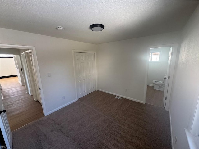 unfurnished bedroom featuring connected bathroom, a closet, a textured ceiling, and dark colored carpet