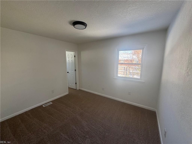 spare room featuring dark colored carpet and a textured ceiling