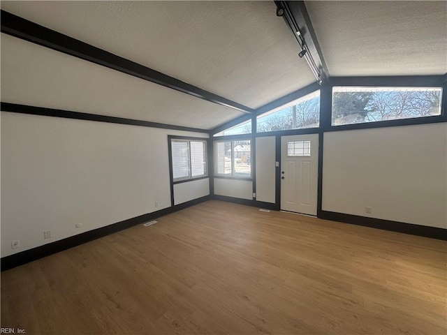 spare room featuring track lighting, vaulted ceiling, and light hardwood / wood-style floors