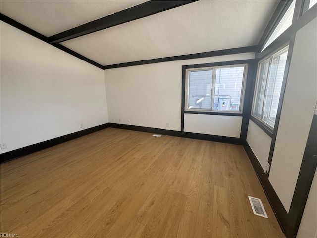 spare room featuring vaulted ceiling with beams and light hardwood / wood-style floors