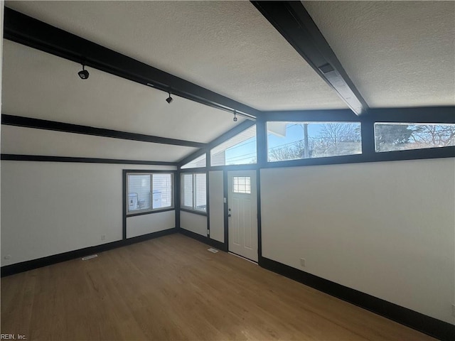 spare room with wood-type flooring, a textured ceiling, track lighting, and lofted ceiling with beams