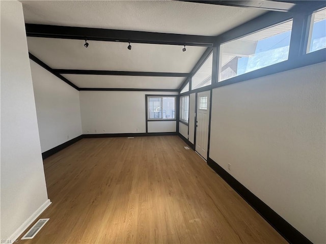 empty room with hardwood / wood-style flooring, vaulted ceiling with beams, and track lighting