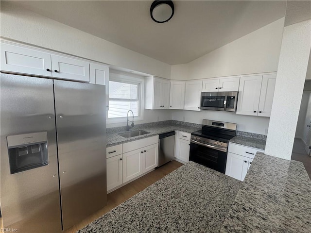 kitchen featuring white cabinets, stainless steel appliances, dark stone countertops, sink, and vaulted ceiling