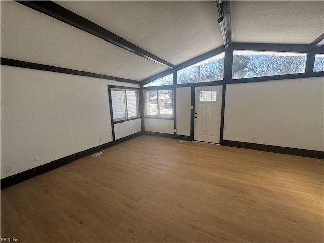 unfurnished room featuring light wood-type flooring, vaulted ceiling with beams, and a textured ceiling