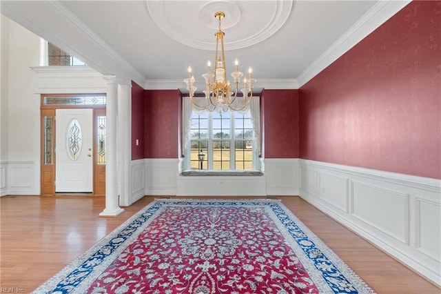 foyer featuring wood-type flooring, crown molding, a chandelier, and ornate columns