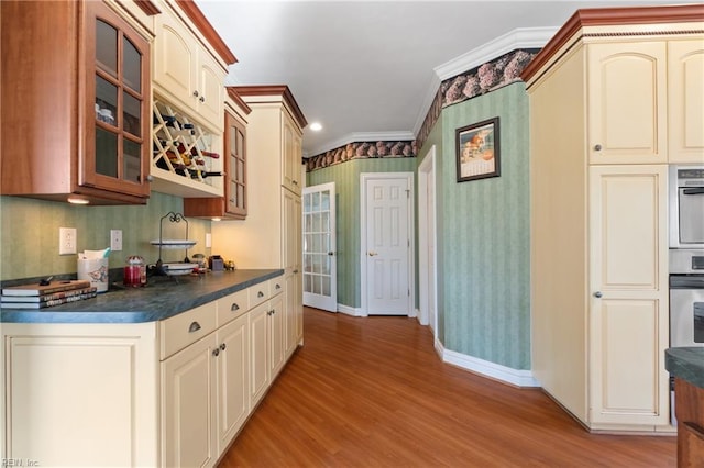 kitchen featuring cream cabinetry, stainless steel oven, light hardwood / wood-style flooring, and ornamental molding