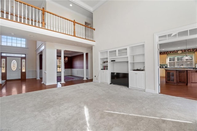 unfurnished living room featuring a towering ceiling, ornamental molding, and dark colored carpet