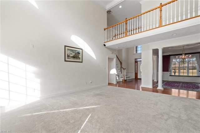 unfurnished living room with an inviting chandelier, ornate columns, a towering ceiling, and carpet flooring