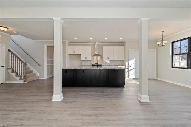 kitchen featuring hardwood / wood-style floors, decorative columns, white cabinetry, ornamental molding, and wall chimney range hood