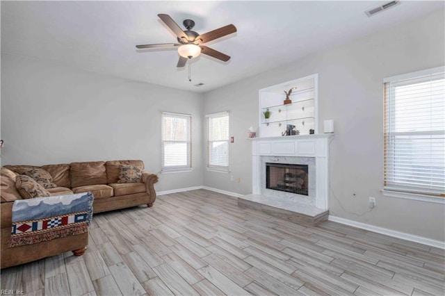 living room featuring ceiling fan, a premium fireplace, and light wood-type flooring