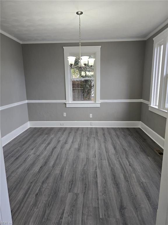 unfurnished dining area featuring dark wood-type flooring, crown molding, and a chandelier