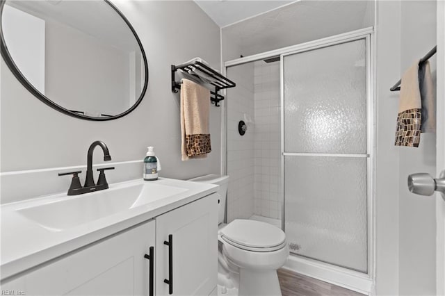 bathroom with hardwood / wood-style floors, a shower with door, toilet, and vanity