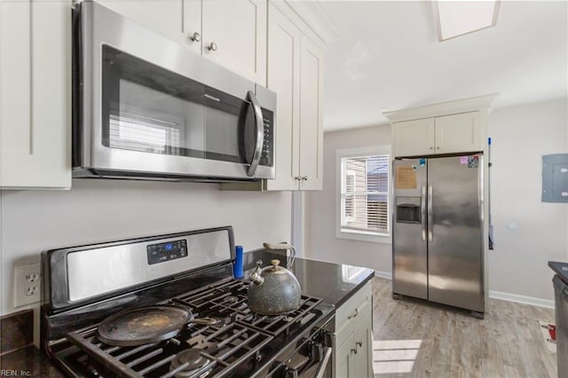 kitchen with appliances with stainless steel finishes, white cabinets, electric panel, light wood-type flooring, and dark stone counters