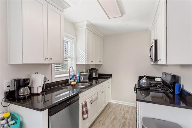 kitchen featuring white cabinetry, stainless steel appliances, dark stone countertops, light hardwood / wood-style floors, and sink