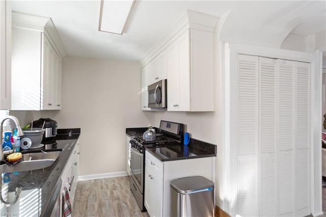 kitchen with appliances with stainless steel finishes, sink, white cabinets, light wood-type flooring, and dark stone counters