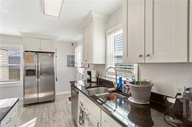 kitchen featuring appliances with stainless steel finishes, white cabinetry, dark stone countertops, sink, and light hardwood / wood-style flooring