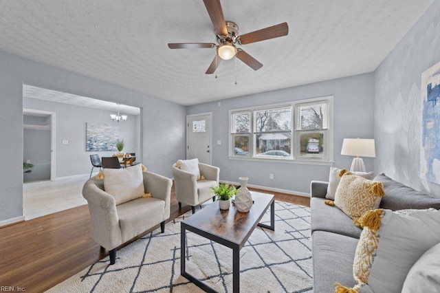 living room featuring light wood-type flooring, ceiling fan with notable chandelier, and a textured ceiling